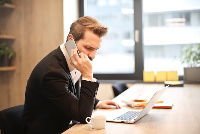 A property manager in a black suit tells a client about their services over the phone